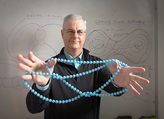 Knot theorist Bill Menasco. The whiteboard in the background depicts drawings of mathematical knots and surfaces that Menasco created from memory. Courtesy of Douglas Levere
