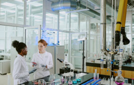 Scientists in white lab coats discussing experimental results in modern, well-equipped laboratory surrounded by various scientific instruments and glassware