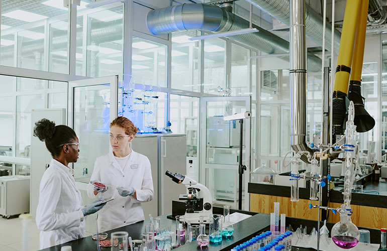 Scientists in white lab coats discussing experimental results in modern, well-equipped laboratory surrounded by various scientific instruments and glassware