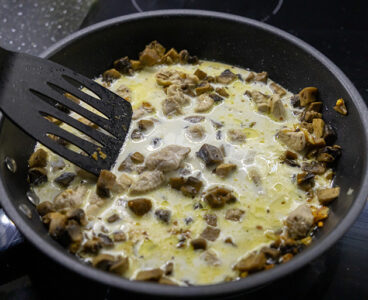 stirring creamy mushrooms and chicken in frying pan with black spatula