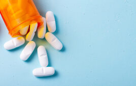 White pills in orange bottle on blue background close up with copy space
