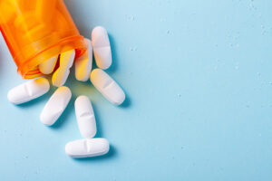 White pills in orange bottle on blue background close up with copy space