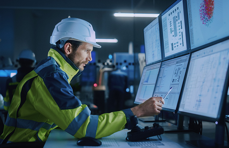 Industry 4.0 Modern Factory: Facility Operator Controls Workshop Production Line, Uses Computer with Screens Showing Complex UI of Machine Operation Processes, Controllers, Machinery Blueprints