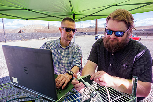 Sandia cybersecurity expert Adrian Chavez (left) and computer scientist Logan Blakely integrate a single-board computer running griDNA's neural-network AI at PNM's Prosperity solar farm test site. The edge-deployable system fuses network traffic and power measurements to detect cyber-physical anomalies. (Photo by Bret Latter)
