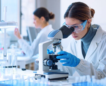 Young scientists conducting research investigations in a medical laboratory, a researcher in the foreground is using a microscope