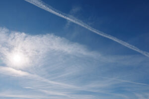 Bright sun over a vast blue sky with contrails and delicate clouds, a peaceful daytime view highlighting atmosphere, light and open sky for creative stock use