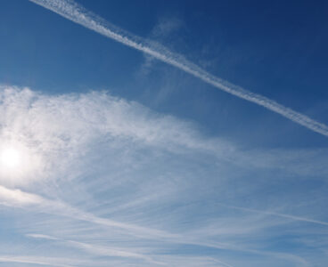 Bright sun over a vast blue sky with contrails and delicate clouds, a peaceful daytime view highlighting atmosphere, light and open sky for creative stock use