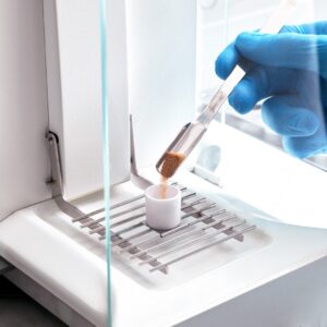 A sample being scooped directly into a ceramic crucible sitting on a balance