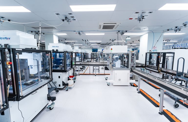 A wider view of Ginkgo Bioworks' automated foundry. Multiple RAC stations feed into shared conveyor infrastructure, the kind of fixed-route "subway" workflow Kelly sees as a stepping stone to fully autonomous labs. [Photo: Ginkgo Bioworks]