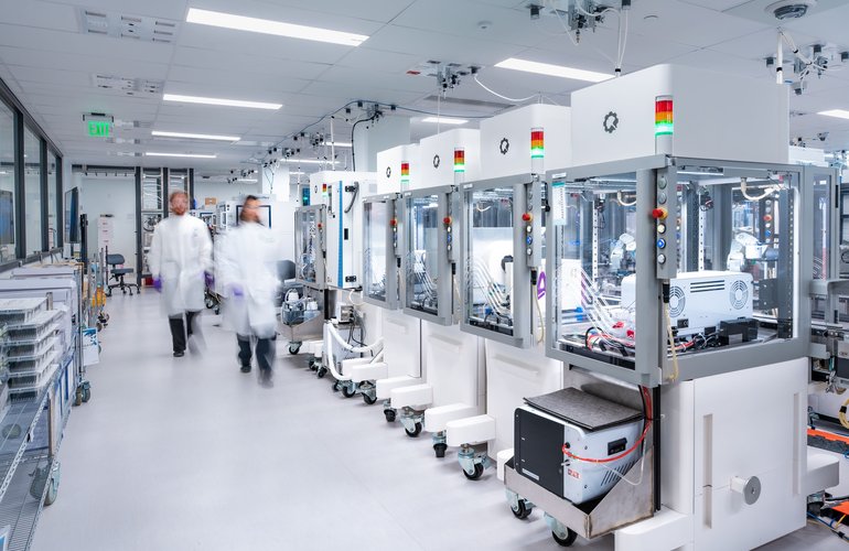 A row of Ginkgo's Reconfigurable Automation Carts, each topped with stack lights signaling run status, as scientists move through the foundry. [Photo: Ginkgo Bioworks]