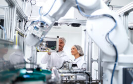 Technology specialists monitoring artificial intelligence of robotic machines inside the factory.