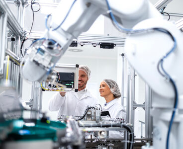 Technology specialists monitoring artificial intelligence of robotic machines inside the factory.