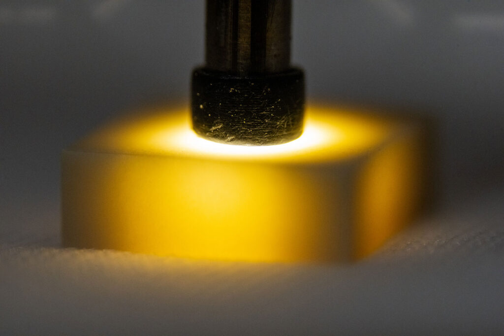 A technician at Sandia manually inspects a ceramic component using a small wand of light and a microscope, a process that can take up to an hour per part and one to two years to learn. The lab's new AI system reduces training time to roughly a week. (Photo by Craig Fritz/Sandia National Laboratories)