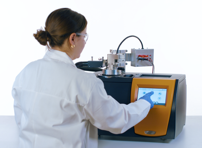 A researcher operates the Waters TA Instruments Coin Cell DSC. The instrument's coin-cell capsule assembly sits atop the DSC furnace, with the electrochemical analysis module visible at upper right. (Credit: Waters Corp.)