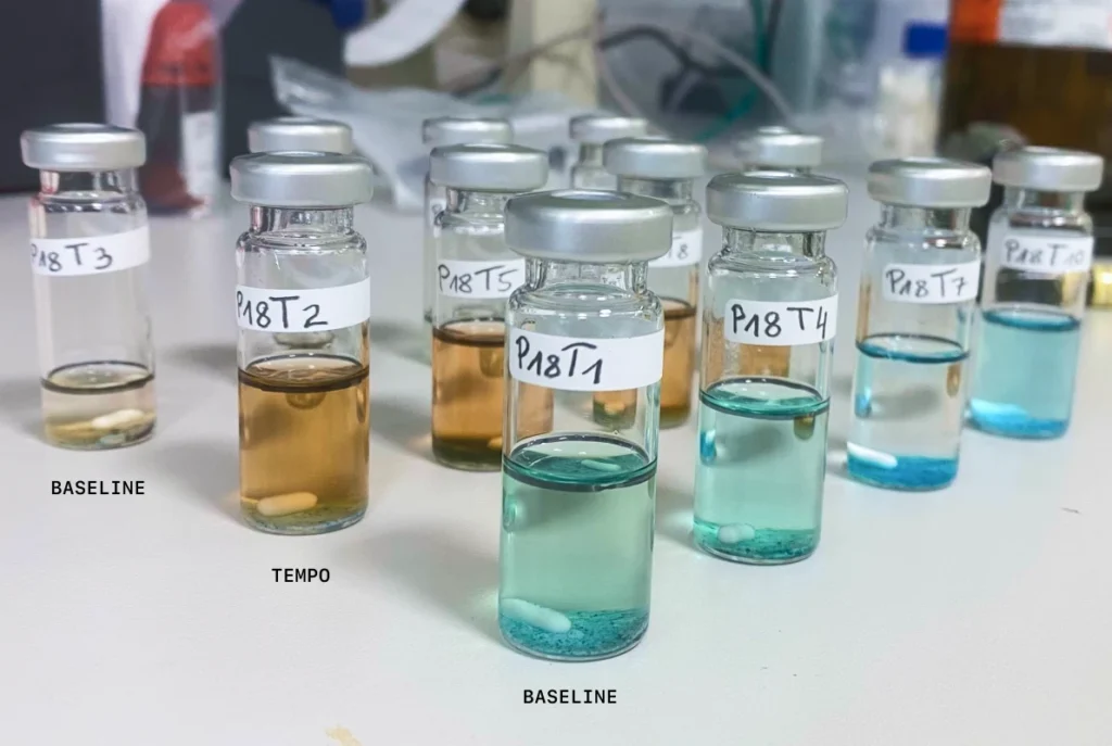 Reaction vials from the manual bench-scale validation, where human chemists repeated representative reactions by hand to confirm the microliter-scale screening results. The vials are labeled by condition, including TEMPO and baseline, no-oxidant runs. Credit: OpenAI/Molecule.one