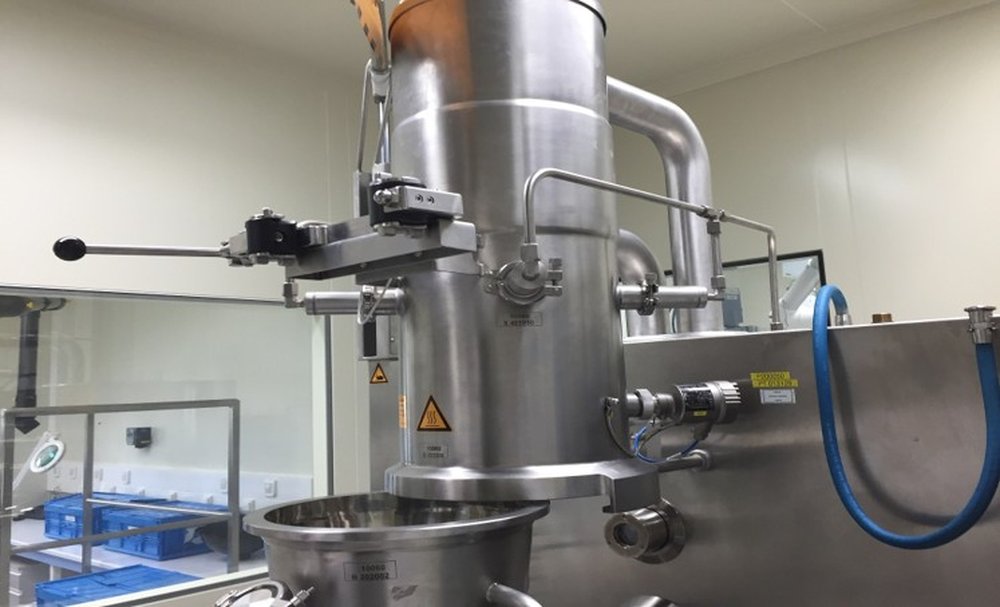 A pharmaceutical spray dryer installed in a cleanroom environment. The transition from lab-scale to commercial spray drying introduces challenges including wall sticking, agglomeration, and particle size distribution changes that can reduce commercial yield.