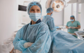 Portrait of surgeon in mask standing in operating room with crossing hands, ready to work on patient