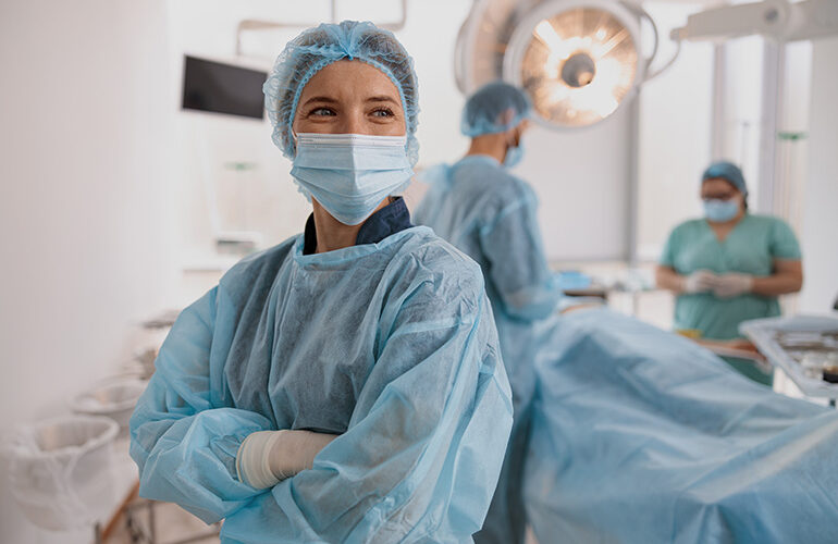 Portrait of surgeon in mask standing in operating room with crossing hands, ready to work on patient