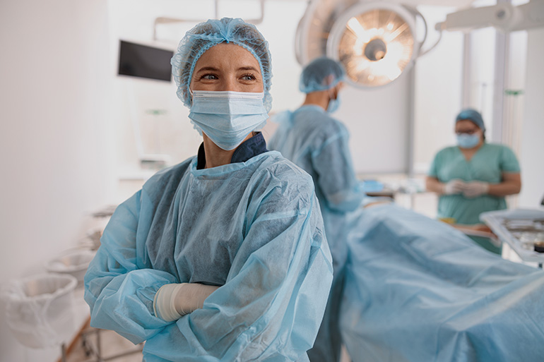 Portrait of surgeon in mask standing in operating room with crossing hands, ready to work on patient