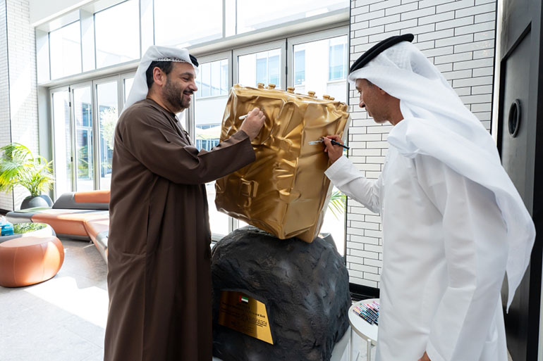 Two signatories add their marks to a gold-wrapped model of TII