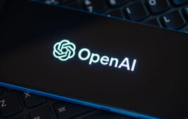 OpenAI logo glowing on a smartphone screen resting on a laptop keyboard