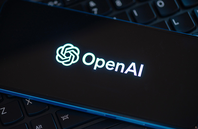 OpenAI logo glowing on a smartphone screen resting on a laptop keyboard